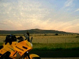 写真: 草原、メサ、夕映えを背にしたバイク