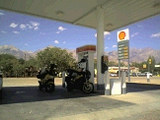 写真: 白い肌の山脈と、給油所に並ぶ二台のバイク
